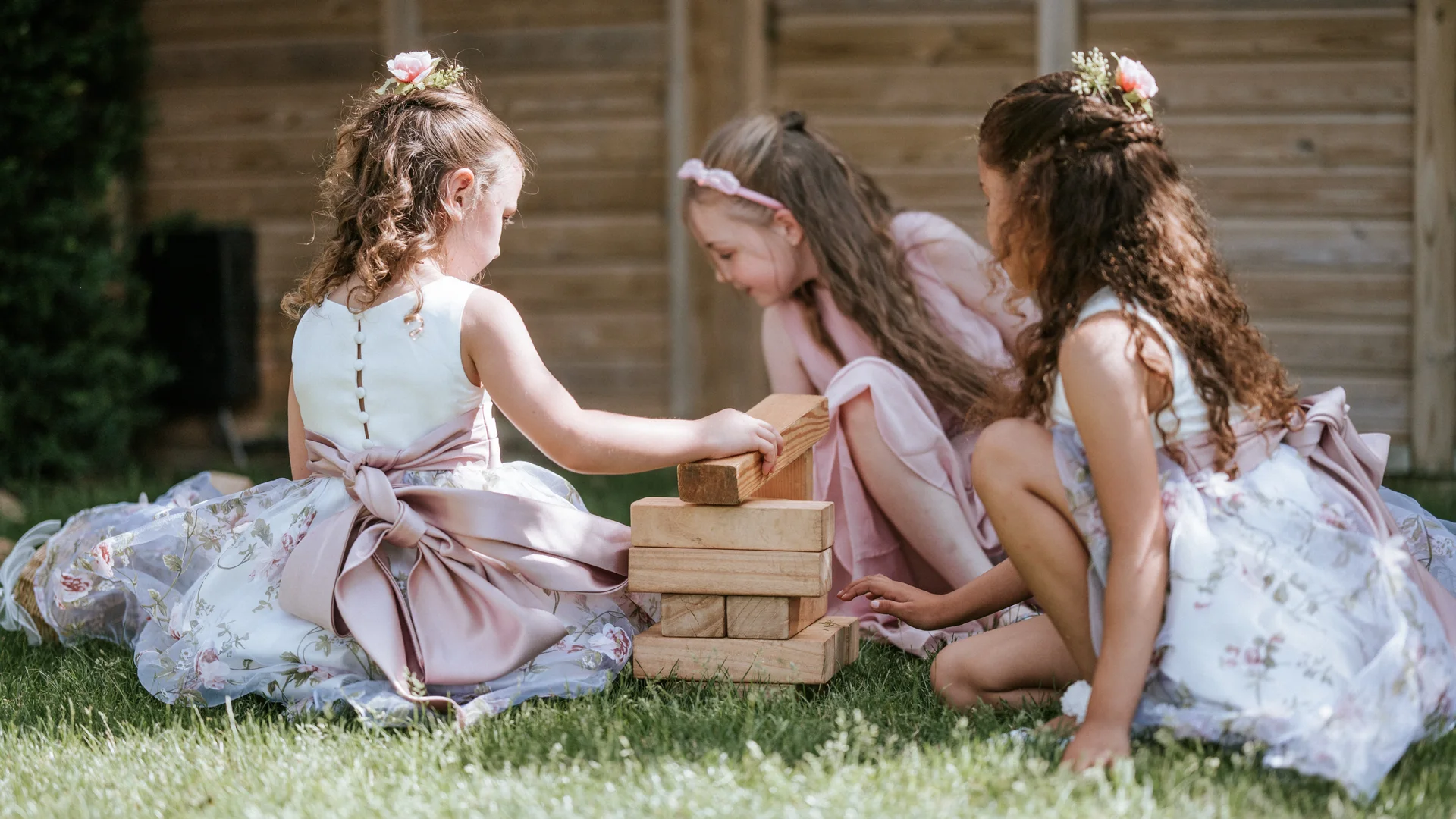 Three flower girls playing giant Jenga on the lawn at a BarnYard wedding