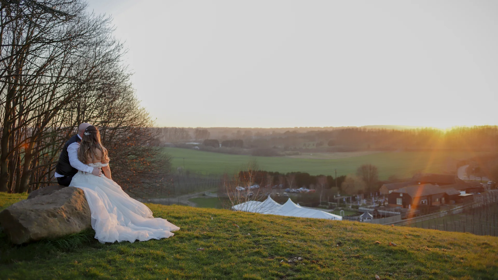 A couple sitting on the hillside above The BarnYard at sunset, looking out over the Kent countryside