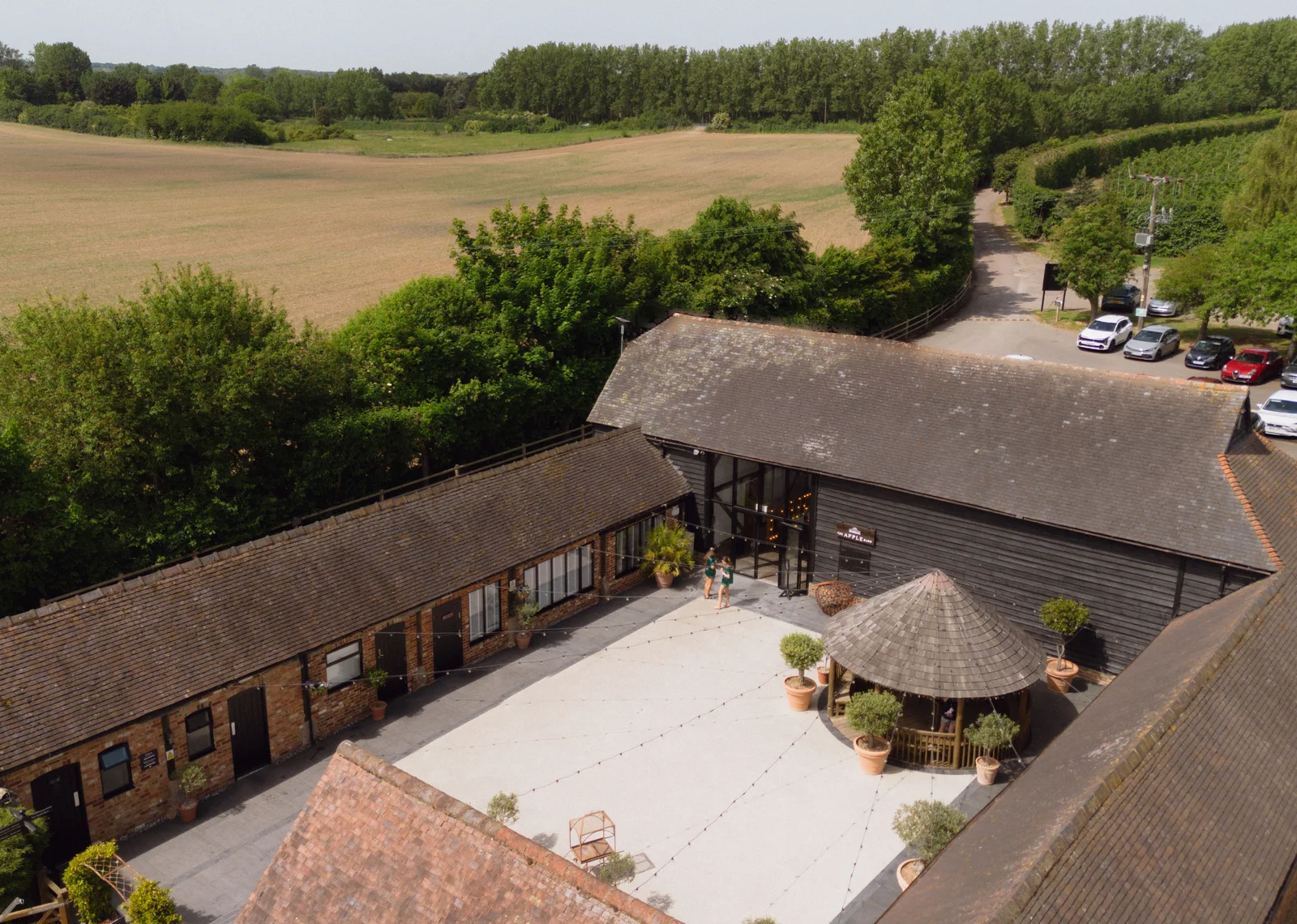 Aerial view of the Courtyard and Apple Barn at The BarnYard, festoon lights strung above the courtyard and the Kent countryside behind